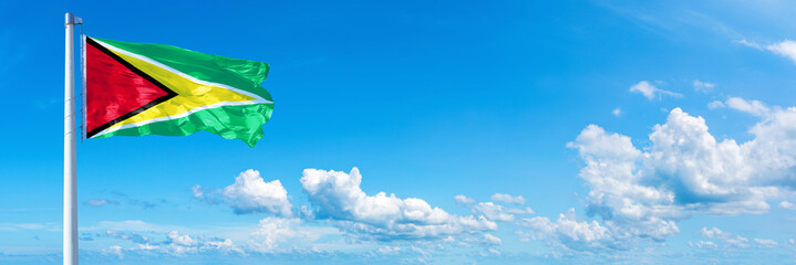 Guyana flag waving on a blue sky in beautiful clouds - Horizontal banner