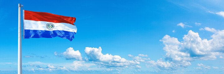 Paraguay flag waving on a blue sky in beautiful clouds - Horizontal banner