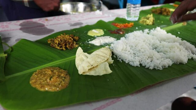 People eating traditional Indian wedding marriage sadhya rice Sambar, parippu dal curry ghee Payasam on banana leaf Onam Vishu Pongal Diwali festival vegetarian food Kerala Tamil Nadu South India.