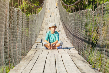 The boy is sitting on the suspension bridge. His eyes are closed. He is resting. (concept of...