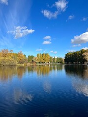 Autumn trees silhouettes reflection on the surface of the lake, blue sky