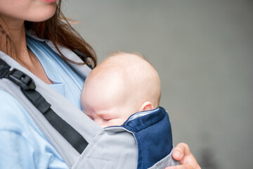 A young mother walks with a baby sleeping in a sling backpack in a green summer park