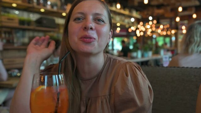 Woman talking and drinking cocktail through the straw in restaurant. 4k video footage in slow motion