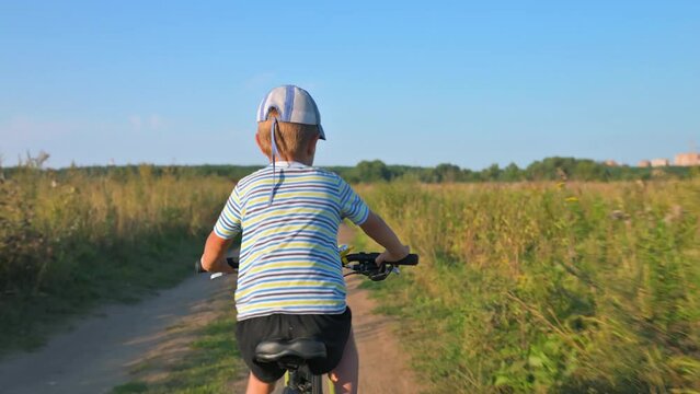 The boy riding his bike on a pathe along the field. 4k video footage in slow motion
