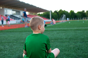 A boy, little sportsmen, sitting on the pinch and waiting for the start of the football match 