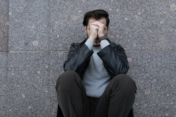 grieving man sitting upset covering his face with his hands