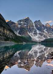 The mountain peaks of the Three Sisters reflected in the calm evening waters of Moraine Lake Canada - 537897953