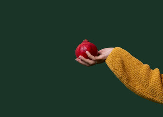 Hand holding red pomegranate against green background. Minimal creative design for autumn fruits, health banner or advertisement.