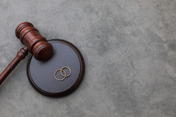 Law theme. Judge gavel wedding rings on concrete stone grey background. Divorce proceedings. Mallet...