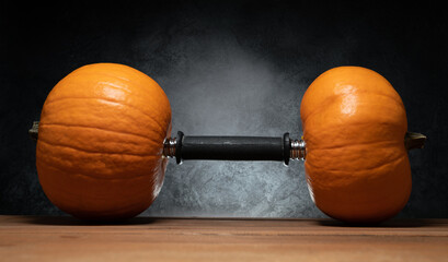 Dumbbell barbell with two orange pumpkins as a weight plates. Gym weightlifting workout and sport training concept. Healthy fitness lifestyle autumn or fall composition for Halloween or Thanksgiving.