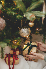 Stylish christmas gift in hands under christmas tree with lights. Merry Christmas and Happy...