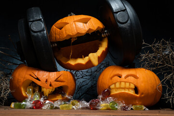 Halloween pumpkin clenching teeth on barbell dumbbell, crushing other carved Jack-o'-lanterns....
