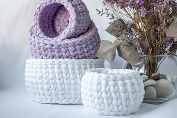 Obraz premium Cute purple and white decorative hand crocheted baskets, sustainable handicraft business, cozy home atmosphere with decorative purple dry plants and white background