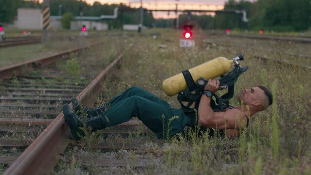 A young muscular man training on the railway tracks and pumps the press by lifting the balloon drager in his hands