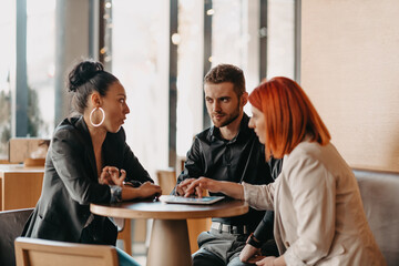 Business people in formal wear sitting coffee and analyzing data. On desk are laptops, graphs, tablets and paperwork.