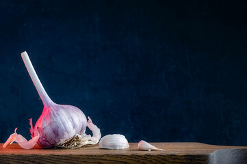 A Whole Bulb Of Garlic And Cloves Lie On A Wooden Board. Kitchen Still Life. Health Care. Natural Product. Traditional Medicine. Dark Background. Place For Text. Selective Focus. Side View.
