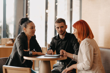 Business people in formal wear sitting coffee and analyzing data. On desk are laptops, graphs, tablets and paperwork.