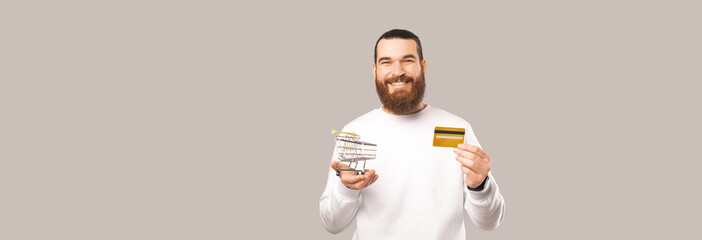Panorama shot of a bearded man holding a credit card and a shopping cart.