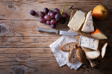 Italian cheese: Pecorino rosso, Blu di bufala, Pecorino toscano, Formaggio al pepe. Cheese platter, with bread, grapes and pear on wooden background, top view, space for text.