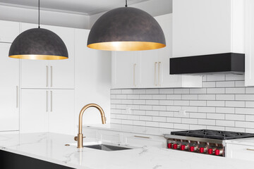 A kitchen sink detail shot with a gold faucet, white cabinets, marble countertop, and subway tile...