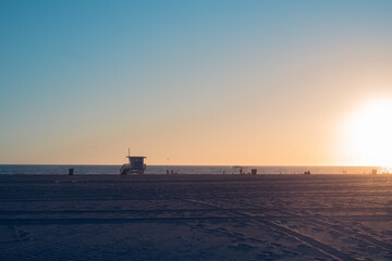Baywatch tower on the beach during sunset with people strolling by