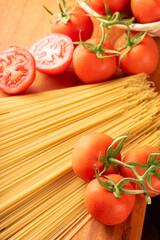 Pasta, beautiful details of red tomatoes and strands of raw spaghetti over rustic wood, selective focus.