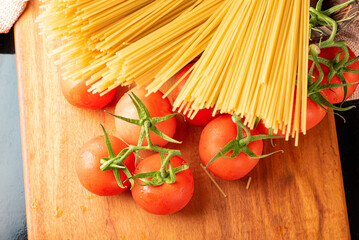 Pasta, beautiful details of red tomatoes and strands of raw spaghetti over rustic wood, top view.