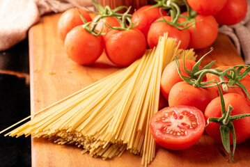Pasta, beautiful details of red tomatoes and strands of raw spaghetti over rustic wood, selective focus.