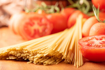 Pasta, beautiful details of red tomatoes and strands of raw spaghetti over rustic wood, selective focus.