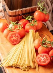 Pasta, beautiful details of red tomatoes and strands of raw spaghetti over rustic wood, selective focus.