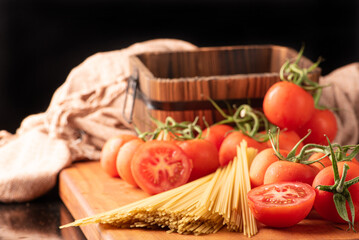 Pasta, beautiful details of red tomatoes and strands of raw spaghetti over rustic wood, selective focus.