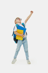 School break. Cheerful mischievous schoolboy in uniform with a backpack jumps on white background....