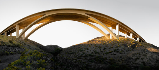 Futuristic arching bridge over the arid desert landscape at sunset
