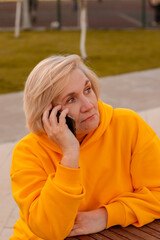 senior aged woman sitting at wooden table outdoor and makes a call