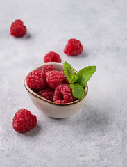 Fototapeta na wymiar Juicy forest raspberry with mint leaf i a bowl on a light textured background. Healthy food concept.