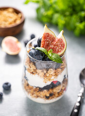 Delicious natural yogurt with muesli, figs and berries in a glass on a blue background close up.