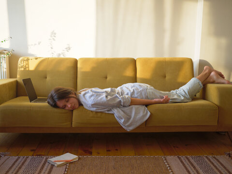 Woman with laptop and notebook lying on the sofa at home