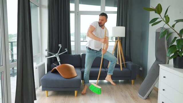 Man cleaning the house and having fun dancing and singing with a broom.