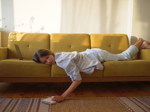 Woman with laptop and notebook lying on the sofa at home