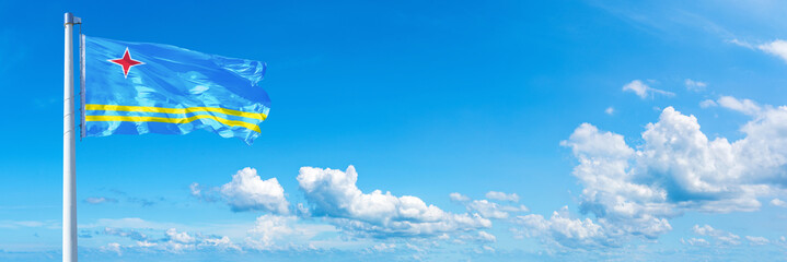 Obraz na płótnie Canvas Aruba flag waving on a blue sky in beautiful clouds - Horizontal banner