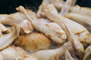 The cook prepares chicken - legs and wings in a cauldron in the open air.