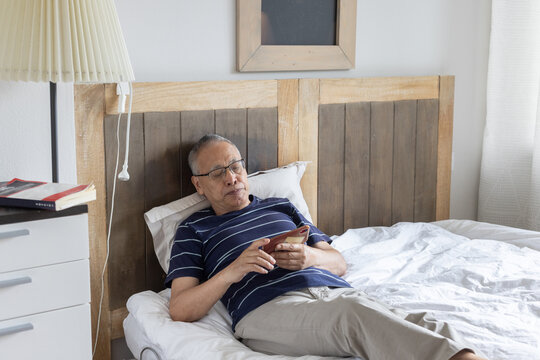 retired man having rest on bed and reading smartphone