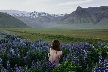 Nude woman standing in purple flower field looking at the mountains