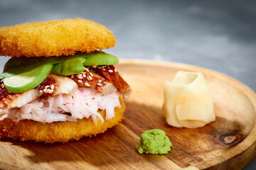 Pan-Asian cuisine concept. Japanese sushi burger made from rice bread, crab meat, avokado and wasabi sauce. Serving on wooden board. copy space