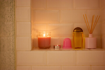 Shower cubicle with water drops on glass. Containers of cosmetics for female body care. Anti-cellulite massage jar. Flames of burning candles. Spa, relaxation at home. Aromatizer diffuser with sticks.