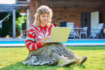 Teenage girl sitting on lawn in backyard, using laptop for studying leisure
