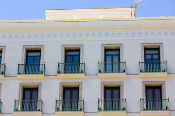 Fototapeta premium Exterior facade. with many windows, balconies, glass doors. Old house wall. Decorated renovated white building in classic style. Architecture on an urban historic street of Europe. Madrid, Spain.