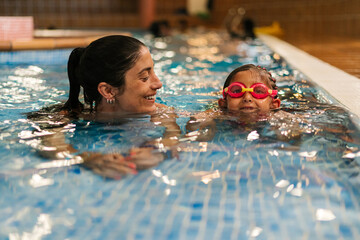 Smiling Hispanic woman with kid swimming in pool