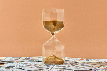 Close up of hourglass placed on bunch of dollars.