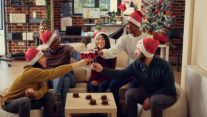 Portrait of diverse people clinking wine glasses during winter party event in office with christmas tree. Coworkers doing toast and saying cheers with alcohol drinks to celebrate xmas eve.